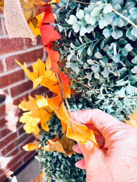 another picture wrapping a fall faux leave vine on the topiary on the porch