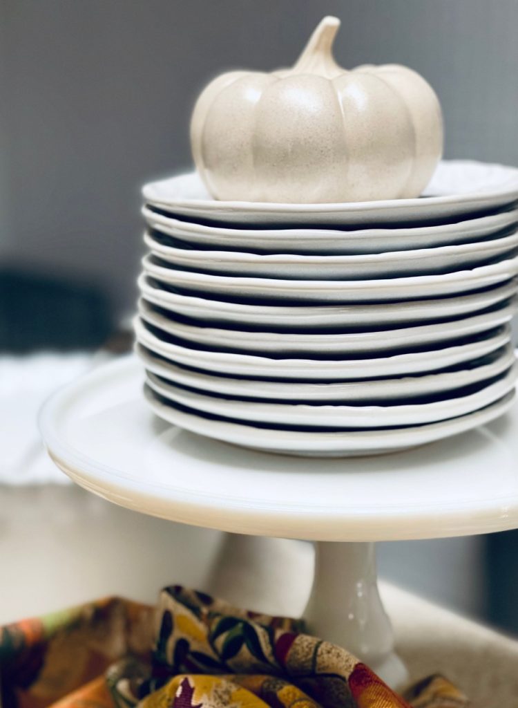 Plates stacked on a cake pedestal on the buffet.